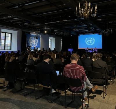 Elever sitter med sina ryggar mot kameran och blickar framat scenen pa FN-rollspelet.