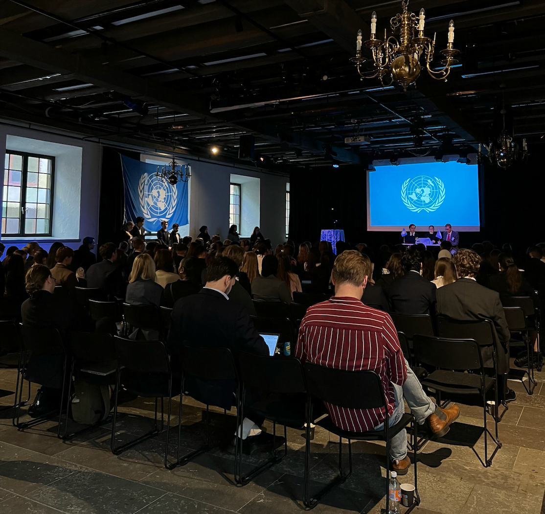 Elever sitter med sina ryggar mot kameran och blickar framat scenen pa FN-rollspelet.