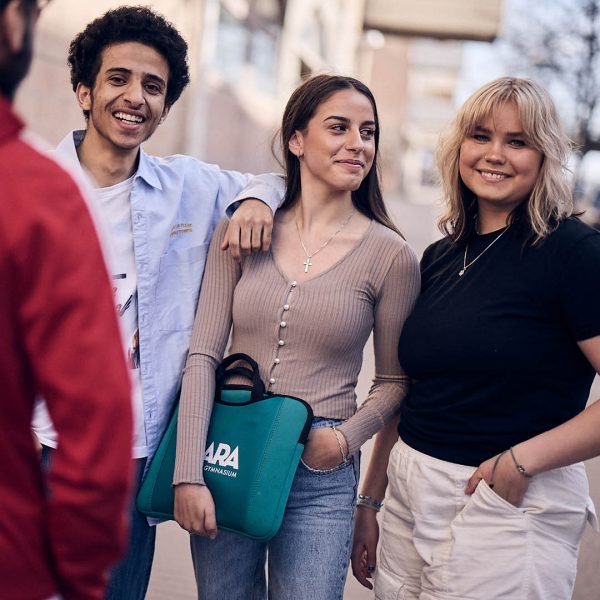 En grupp elever star tillsammans utomhus och kollar in i kameran.