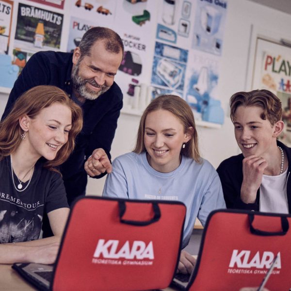 Elever och larare kollar pa en laptop