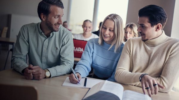 Elever och larare sitter i ett klassrum och pratar vid en bank.