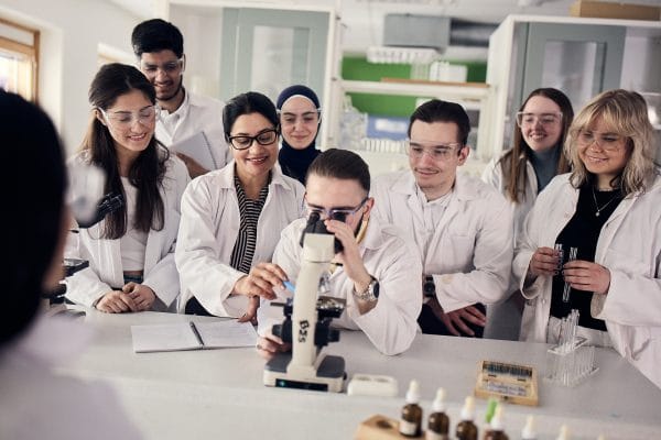 En stor grupp elever genomfor ett experiment i naturkunskap tillsammans med en larare.