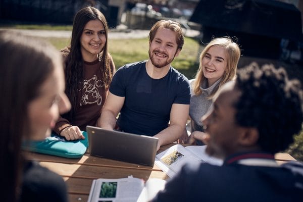 Nagra elever sitter utomhus med ett grupparbete.
