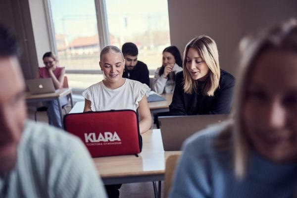 Tva elever sitter i ett ljust klassrum framfor sina datorer.