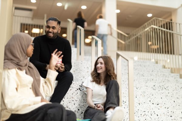 Tre glada elever sitter i en ljus trappa i skolan pa rasten.